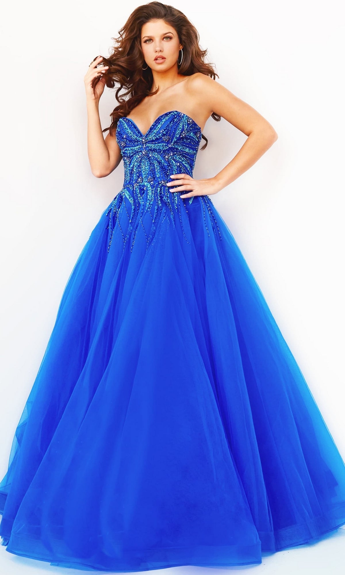 A woman wearing the Jovani Strapless Sweetheart Long Prom Gown 07946, featuring a beaded blue bodice and full tulle skirt, stands against a plain white background.